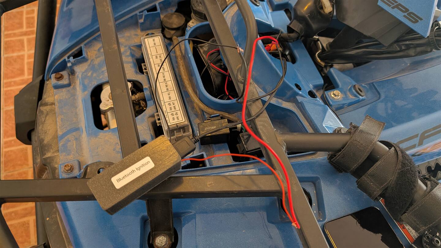 A Keyvo development unit, labelled Bluetooth Ignition, cable-tied beside the fuse box of a blue CFMoto ATV with its body panel removed.